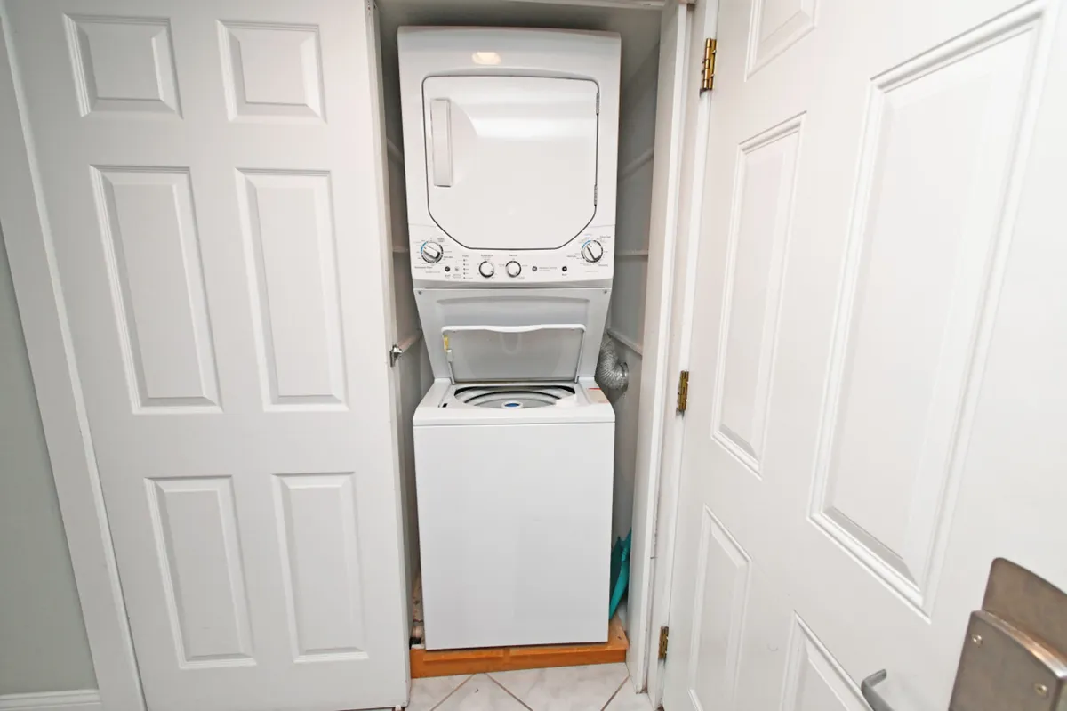 A neatly organized laundry closet featuring a stacked washer and dryer, bi-fold doors open to reveal convenient in-unit laundry amenities. The surrounding area is clean and efficient, underscoring ease for guests during their stay.